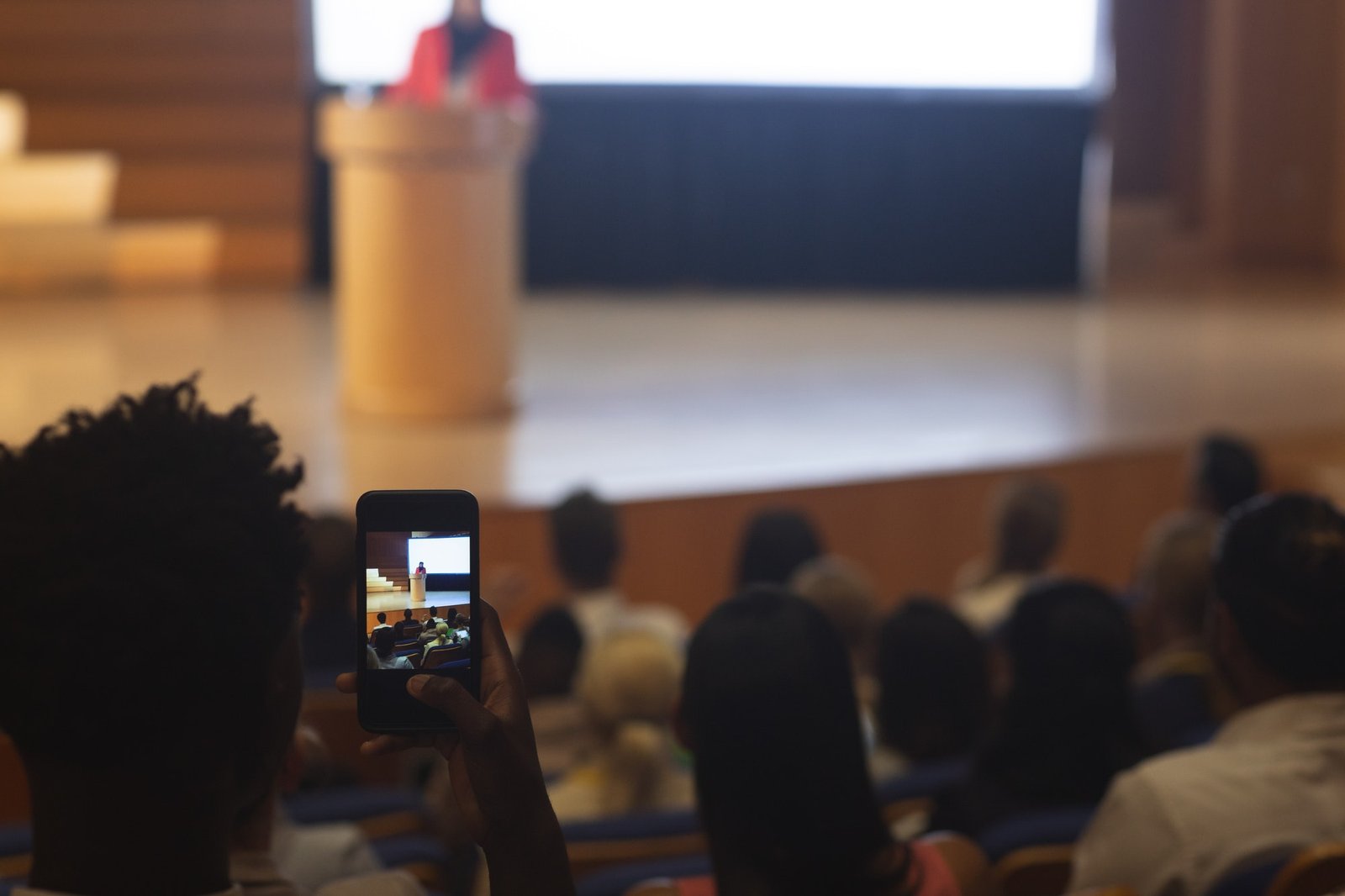 Man with smartphone taking video of businesswoman in the auditorium